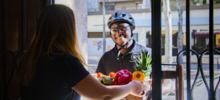 Coursier à vélo livrant un panier de fruits et légumes à domicile.