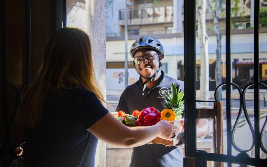 Coursier à vélo livrant un panier de fruits et légumes à domicile.